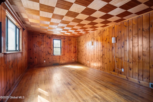 empty room with visible vents, wooden walls, and wood-type flooring