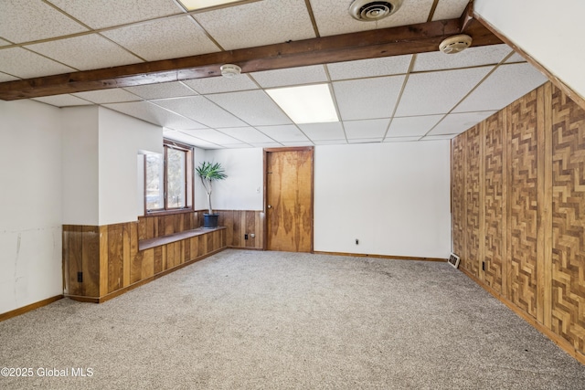 unfurnished room featuring visible vents, a drop ceiling, wooden walls, carpet, and wainscoting