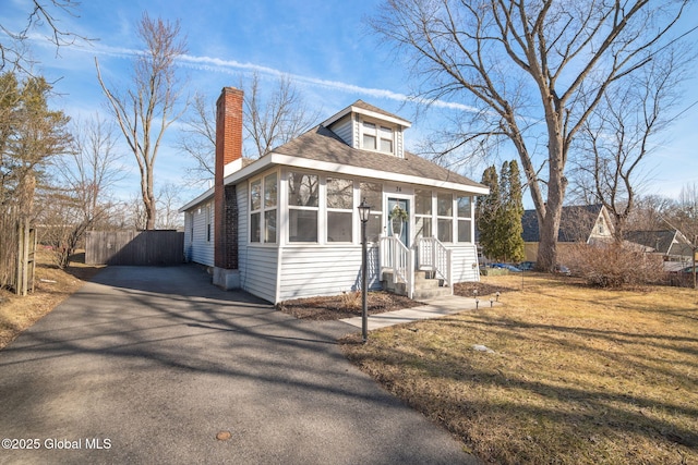 view of front of home with a shingled roof, a front lawn, a chimney, a sunroom, and driveway