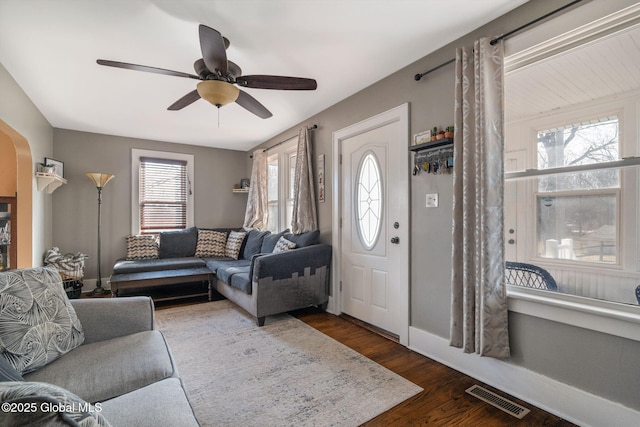 living room with visible vents, baseboards, a ceiling fan, and dark wood-style flooring