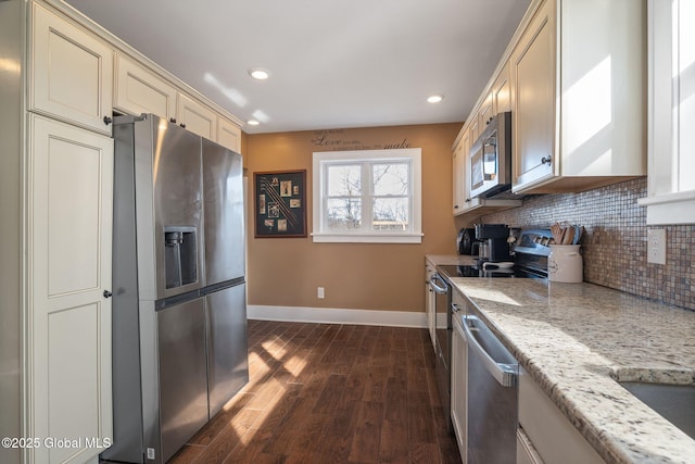 kitchen featuring dark wood-type flooring, baseboards, decorative backsplash, appliances with stainless steel finishes, and cream cabinetry