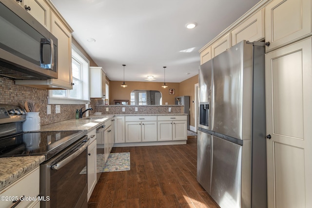 kitchen featuring cream cabinetry, a sink, appliances with stainless steel finishes, a peninsula, and decorative backsplash