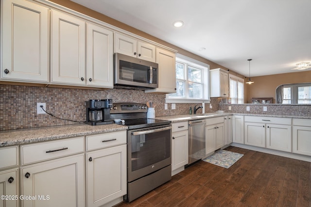 kitchen featuring dark wood-style floors, a sink, decorative backsplash, hanging light fixtures, and stainless steel appliances