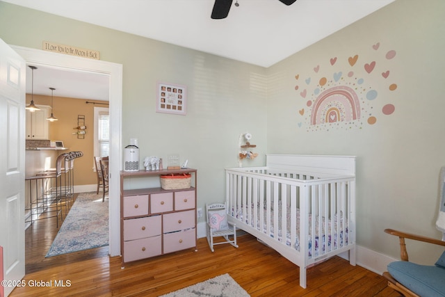 bedroom with a crib, baseboards, wood-type flooring, and ceiling fan