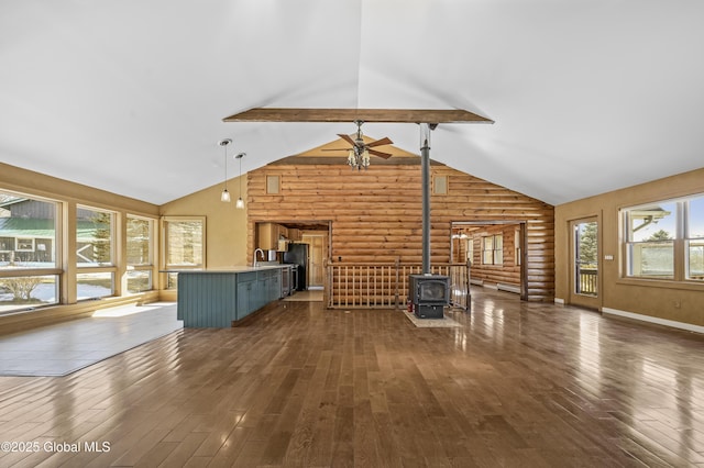 unfurnished living room featuring dark wood-type flooring, ceiling fan, beam ceiling, a wood stove, and log walls