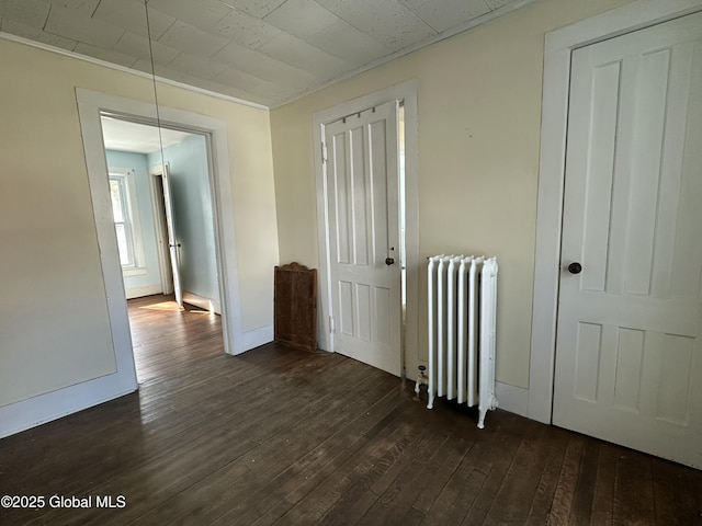 unfurnished bedroom with radiator, dark wood-style floors, and baseboards