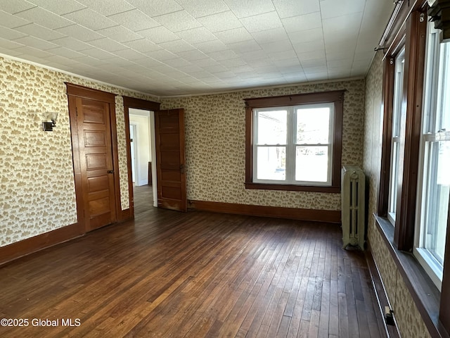 spare room featuring dark wood-style floors, radiator, wallpapered walls, and baseboards