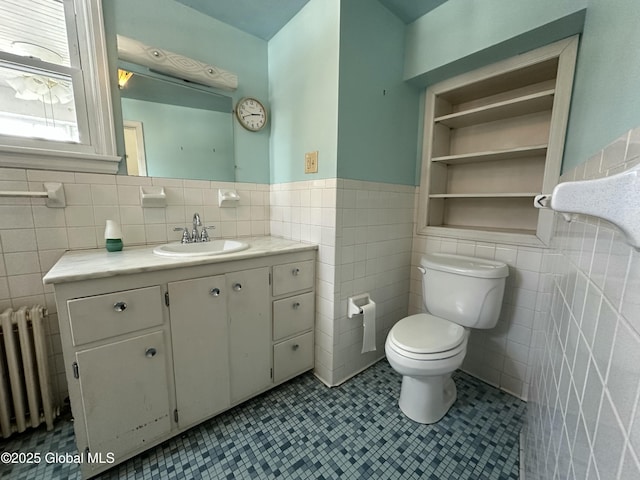 bathroom with radiator, a wainscoted wall, toilet, vanity, and tile walls