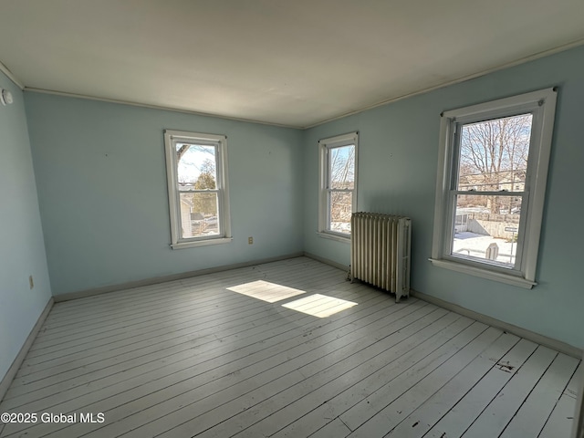 unfurnished room featuring baseboards, plenty of natural light, radiator, and light wood finished floors