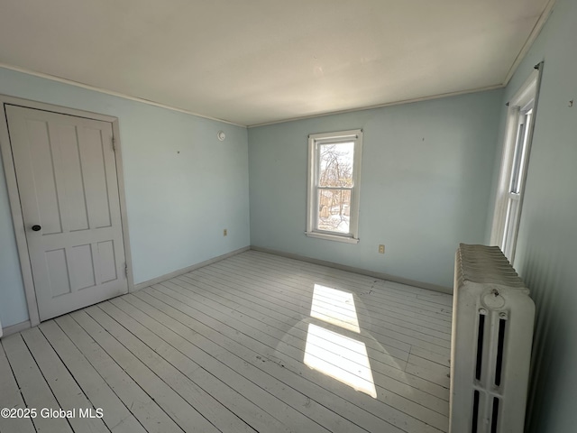 spare room with crown molding, radiator, baseboards, and light wood finished floors