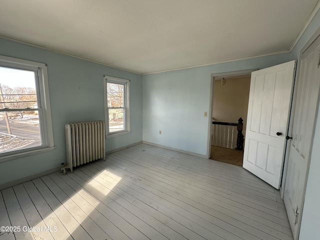 empty room featuring light wood-style flooring, radiator, and baseboards