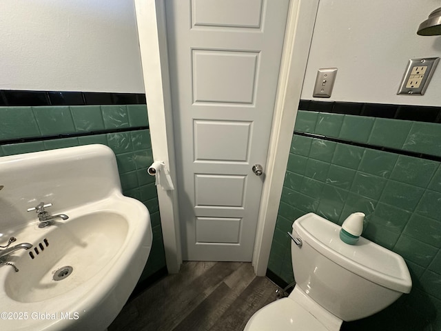 half bath featuring a sink, toilet, tile walls, and wood finished floors