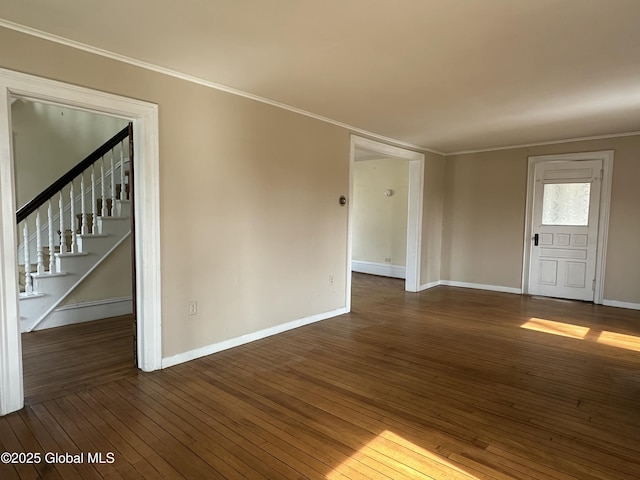 spare room featuring dark wood finished floors, crown molding, stairs, and baseboards