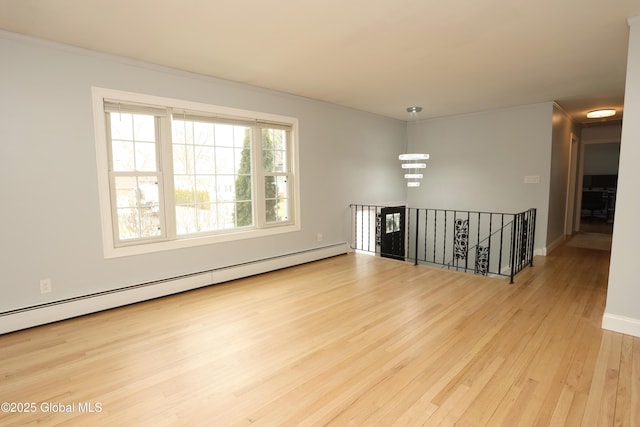 spare room featuring baseboards, a baseboard heating unit, an inviting chandelier, and wood finished floors