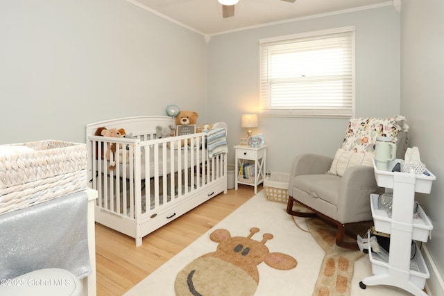 bedroom featuring a ceiling fan, crown molding, a nursery area, and wood finished floors