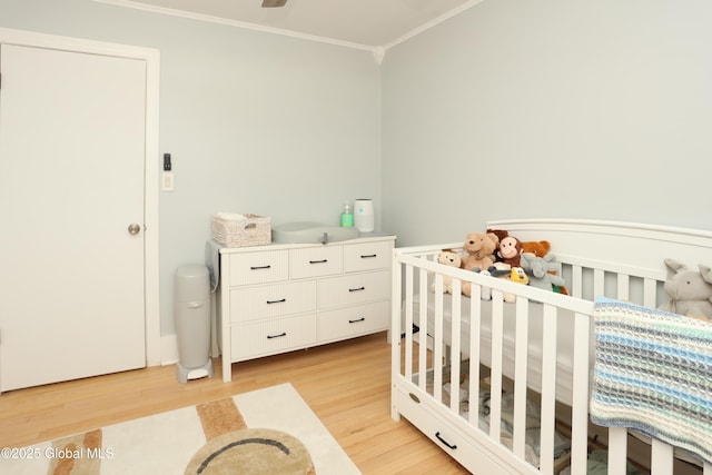 bedroom with light wood-style flooring, a crib, and crown molding