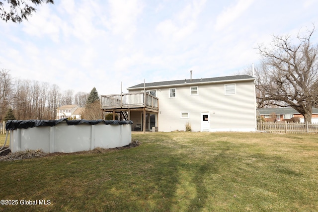 back of house featuring a covered pool, a lawn, a wooden deck, and fence