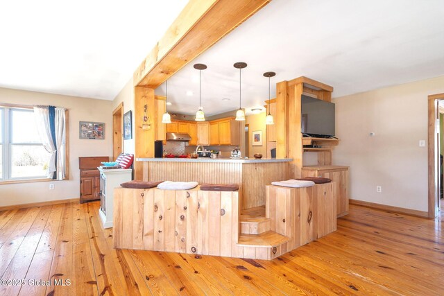 kitchen with under cabinet range hood, decorative light fixtures, a peninsula, light wood finished floors, and baseboards