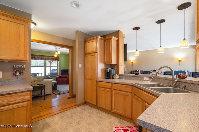 kitchen with decorative light fixtures, a peninsula, light countertops, and a sink