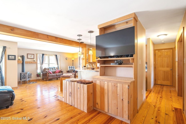 kitchen with light wood-style flooring, open floor plan, a peninsula, a wood stove, and hanging light fixtures