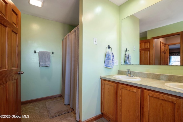 full bath with a sink, curtained shower, baseboards, and double vanity