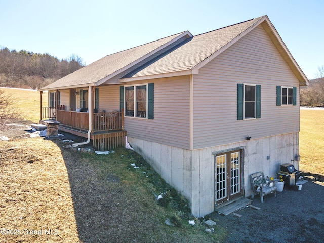 view of property exterior with a porch, french doors, a lawn, and a shingled roof