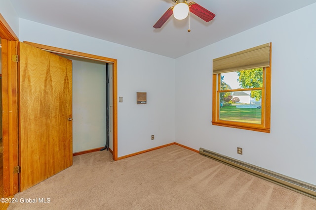 unfurnished room with a baseboard heating unit, light colored carpet, baseboards, and a ceiling fan