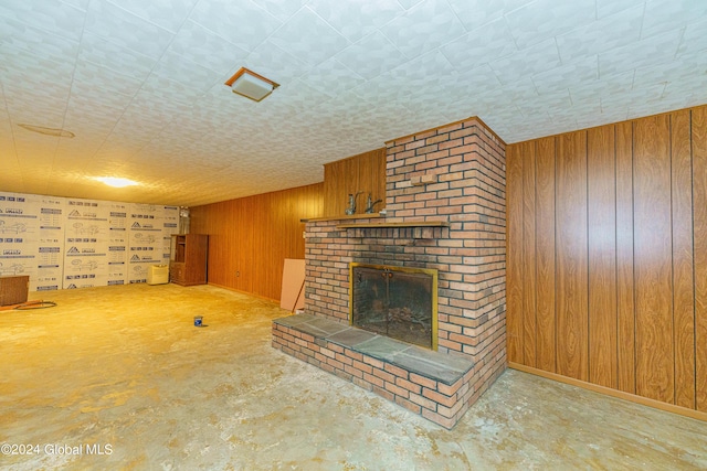 unfurnished living room with a fireplace, concrete flooring, and wood walls