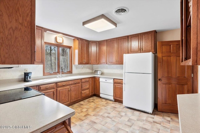 kitchen featuring decorative backsplash, white appliances, brown cabinetry, and visible vents