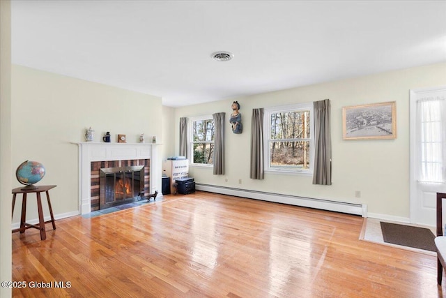 living area with visible vents, a fireplace with flush hearth, baseboard heating, and wood finished floors