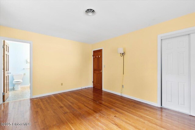 unfurnished bedroom with visible vents, connected bathroom, baseboards, and light wood-style floors