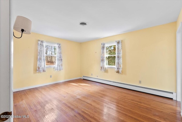 empty room featuring visible vents, plenty of natural light, a baseboard heating unit, and wood finished floors