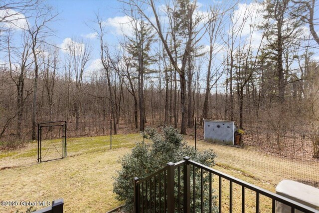 view of yard with an outbuilding, a wooded view, a storage unit, and a gate