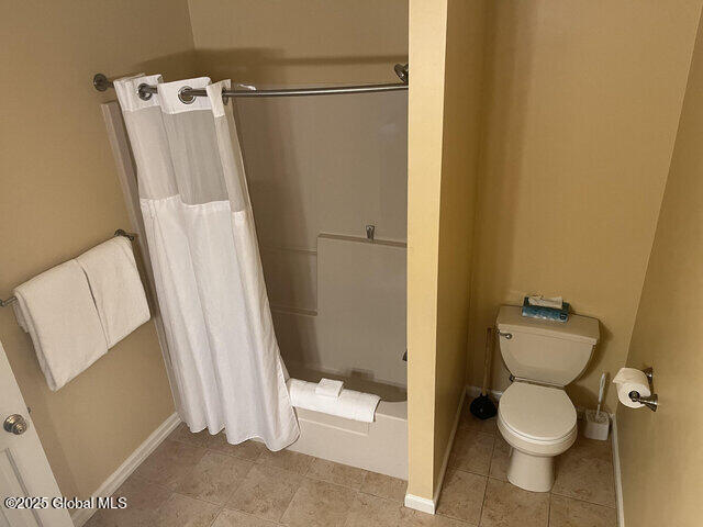 full bath featuring shower / bathtub combination with curtain, baseboards, toilet, and tile patterned flooring