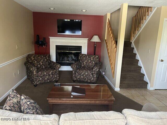 living room featuring baseboards, a glass covered fireplace, stairs, and tile patterned flooring