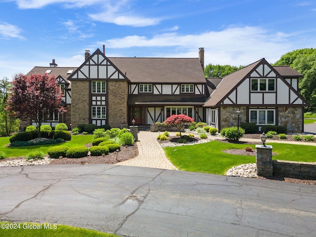 view of front of house featuring stone siding, stucco siding, a chimney, and a front lawn