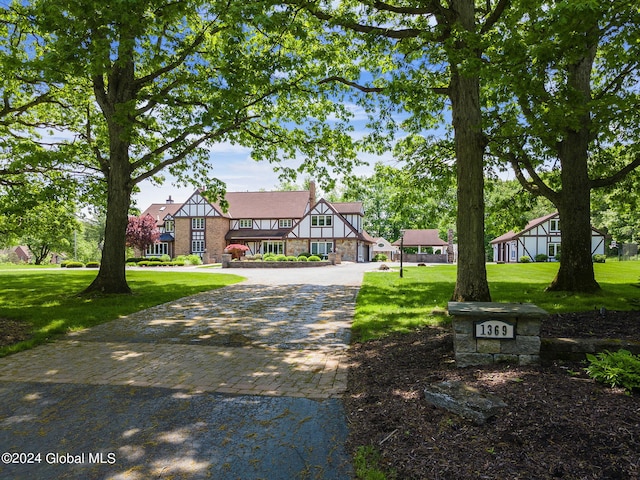 tudor house with stone siding, decorative driveway, and a front lawn