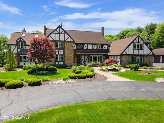 english style home featuring a front yard, stone siding, and a chimney