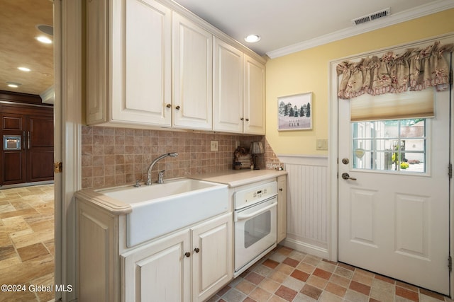 kitchen featuring oven, visible vents, wainscoting, crown molding, and light countertops