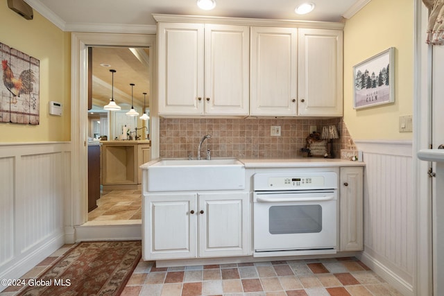 kitchen featuring a sink, light countertops, crown molding, wainscoting, and white oven