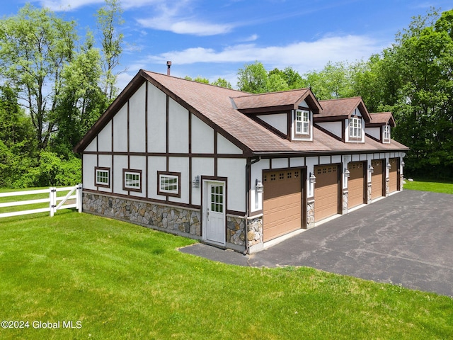 tudor-style house featuring a front yard, fence, a shingled roof, stucco siding, and a garage