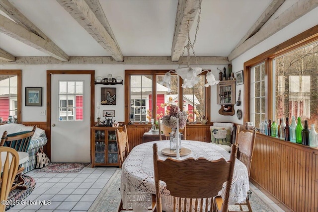 dining room with beamed ceiling, light tile patterned flooring, and wainscoting