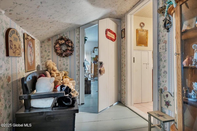 hall with wallpapered walls and lofted ceiling