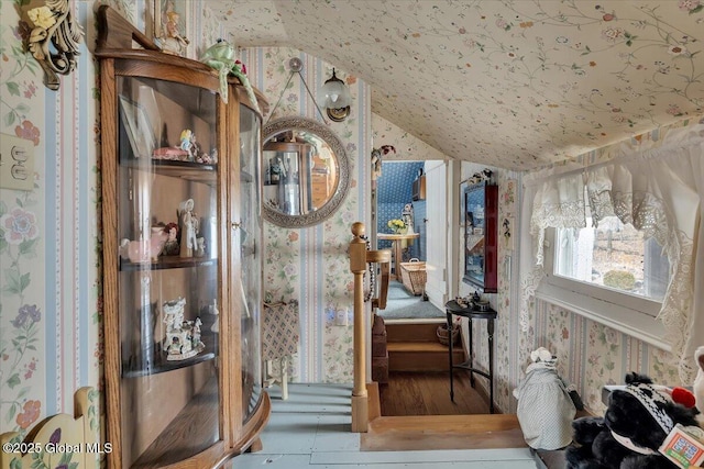 interior space with wood finished floors, wallpapered walls, and vaulted ceiling