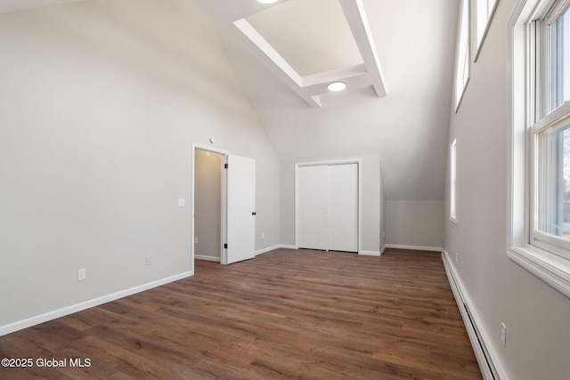 spare room featuring a baseboard heating unit, baseboards, high vaulted ceiling, and wood finished floors