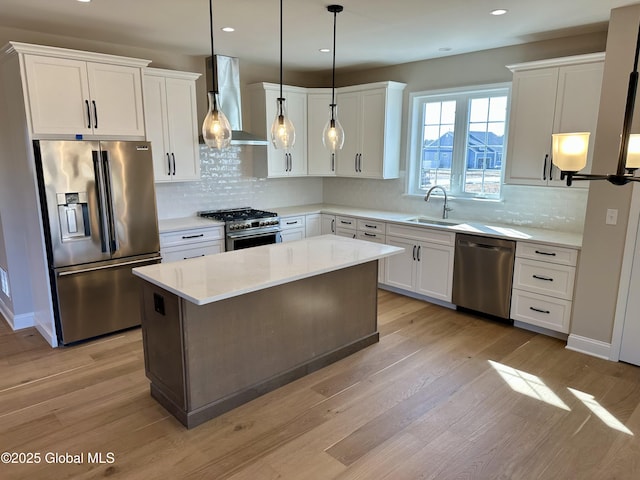 kitchen with a sink, light wood-type flooring, appliances with stainless steel finishes, and wall chimney exhaust hood