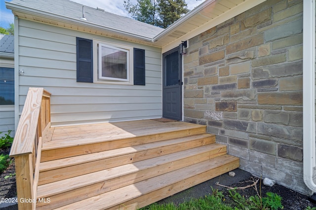 doorway to property with stone siding and a shingled roof