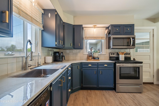 kitchen with light wood-type flooring, a sink, blue cabinetry, appliances with stainless steel finishes, and decorative backsplash