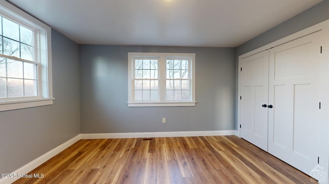 unfurnished bedroom featuring wood finished floors, baseboards, and a closet