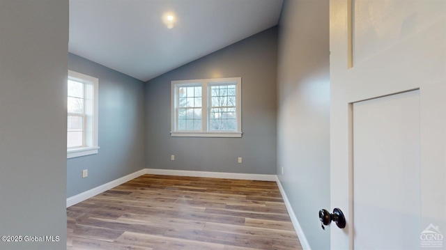 spare room featuring baseboards, wood finished floors, and vaulted ceiling